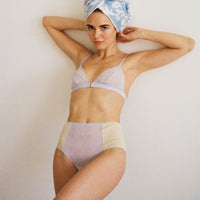 Woman standing , leaning against a wall with. a towel wrapped around her hair. She is wearing the Semiromantic Bea high waist pantie and Esme triangle bra in color Mist