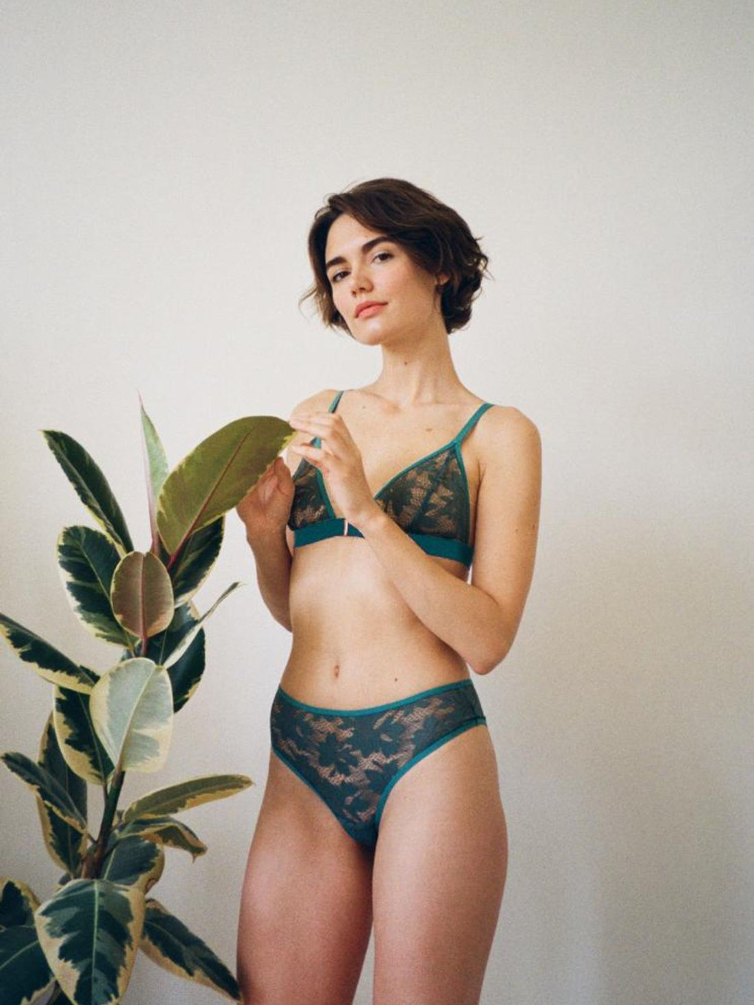 Model standing next to plant wearing Semiromantic Lingerie set made from Green lace.